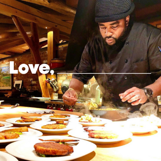 A chef wearing a black jacket and hat is leaning over plates set out on a table